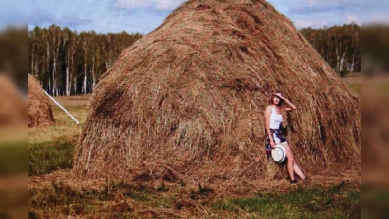 Блондинка в шляпе сидит на стоге сена